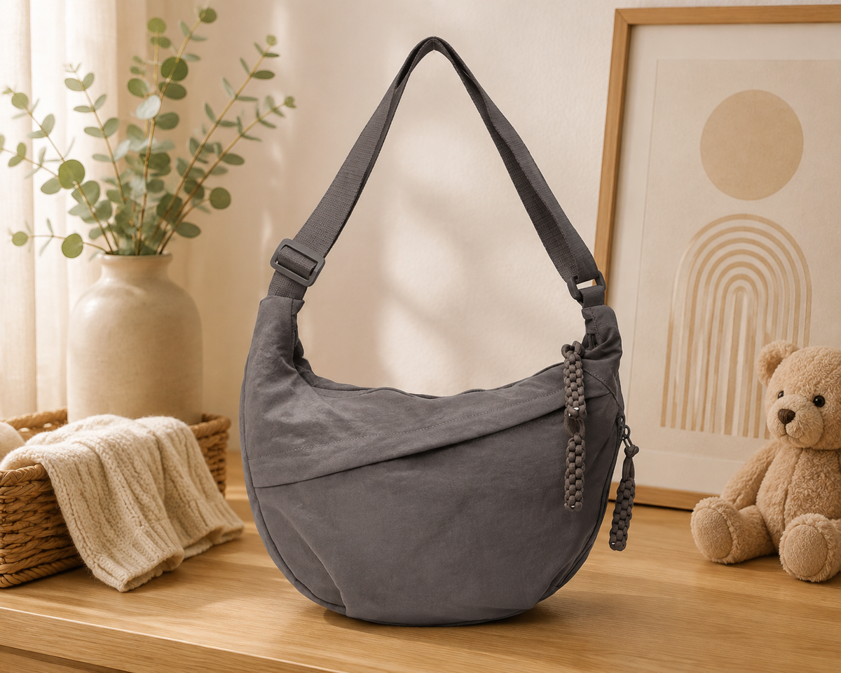 Sac à langer bandoulière, en toile, gris, posé dans un intérieur clair aux tons naturels