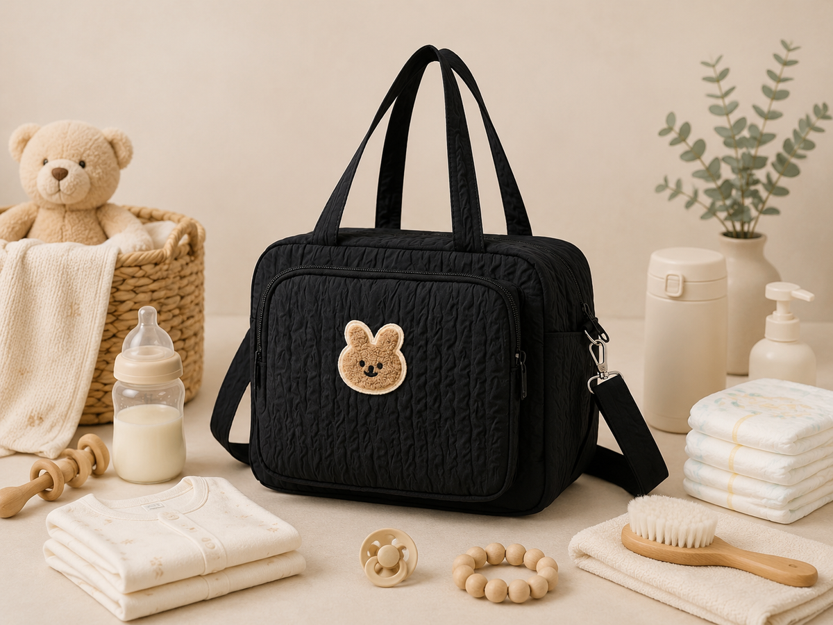Sac à langer bandoulière matelassé, écusson lapin, noir, posé dans un intérieur clair aux tons naturels